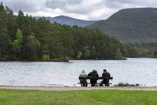 Rothiemurchus'ta deniz kenarında bir bankta oturan üç kişi.